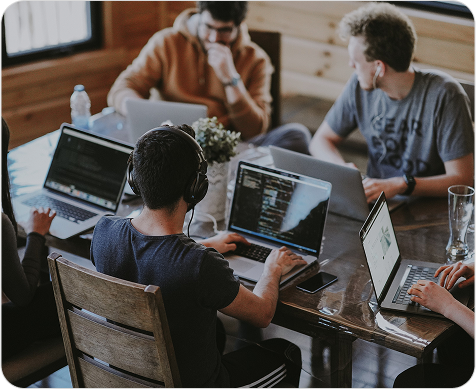 A group of people working on laptops around a table in what appears to be a co-working space or cafe.